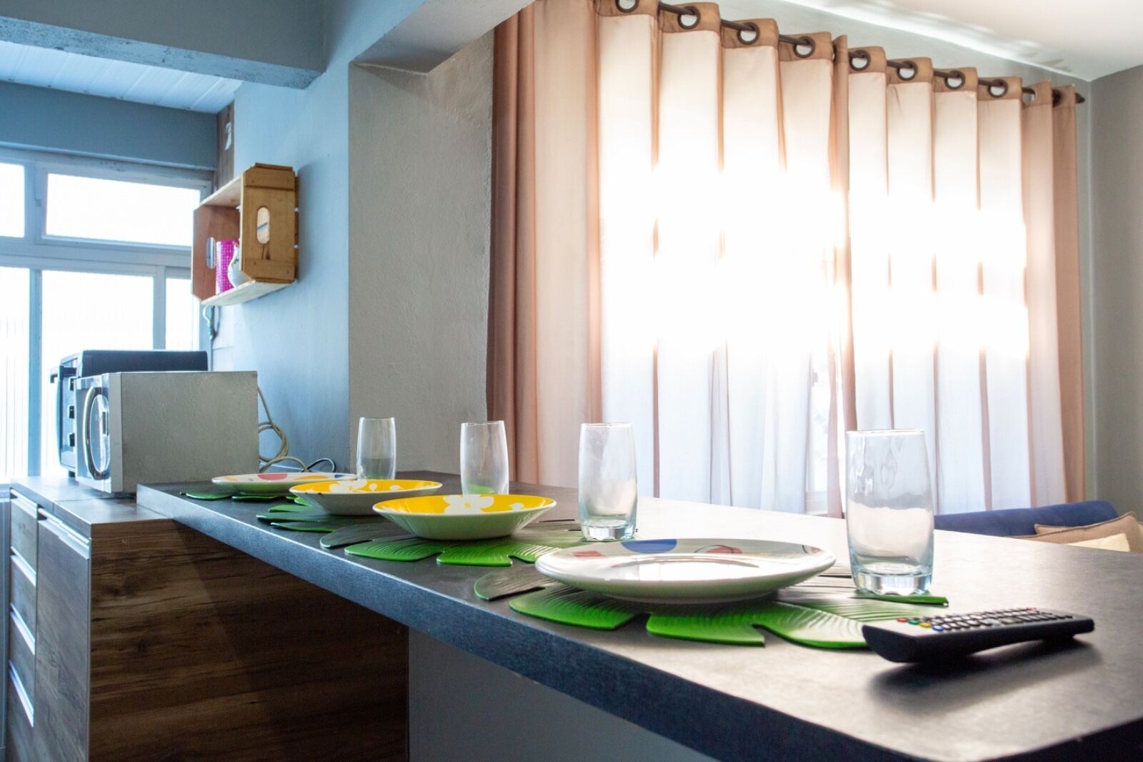 A kitchen counter with a microwave, a toaster, and a coffee maker. There are plates, glasses, and a remote control on the counter.