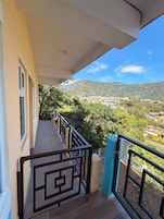 Un balcón con vistas a un pueblo en la ladera y zonas verdes.
