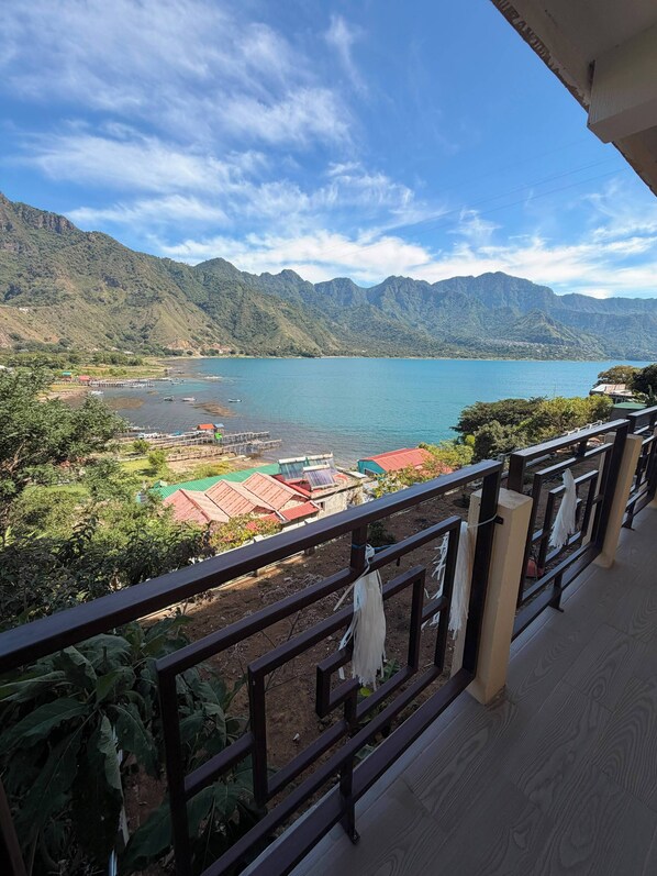 A balcony with a view of a lake, mountains, and a dock with boats.