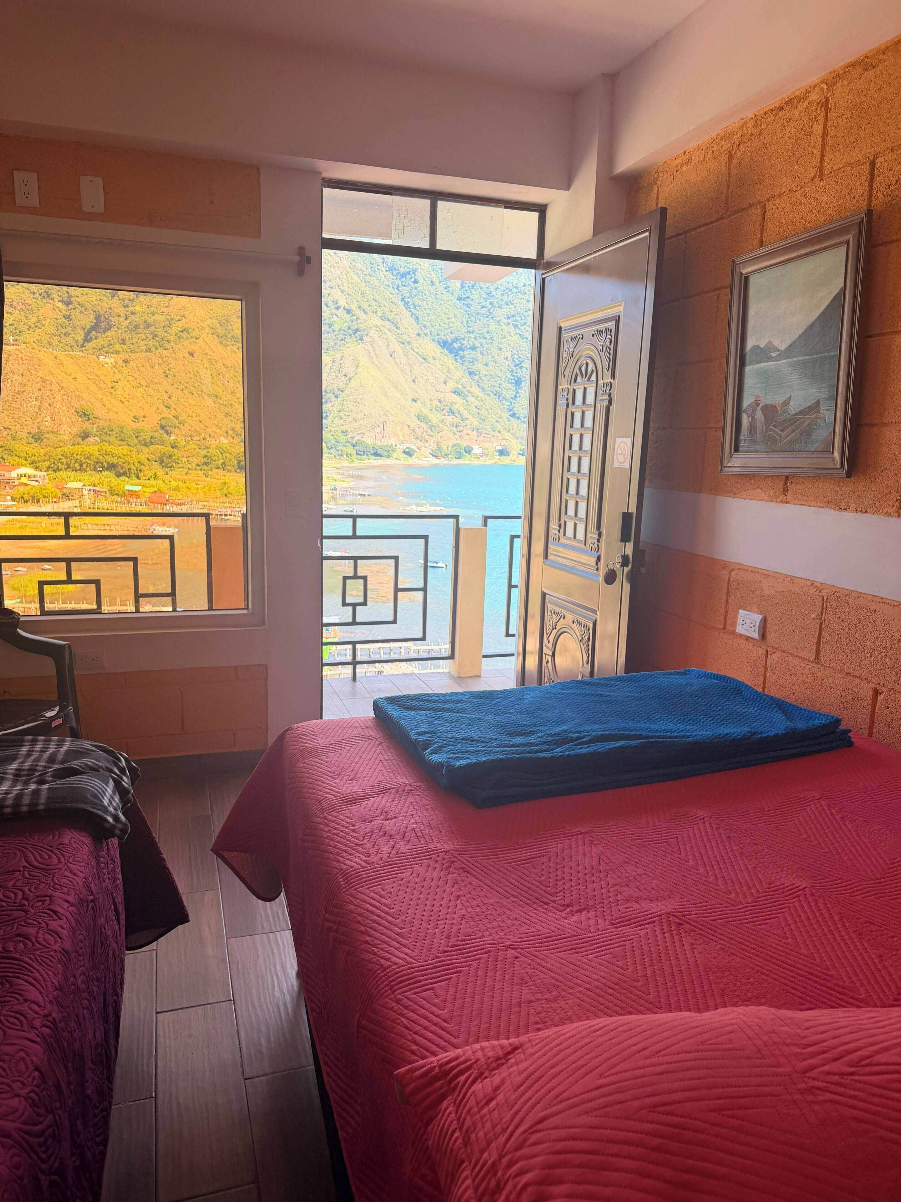 A hotel room with a bed, a chair, a view of a lake, and a mountain.
