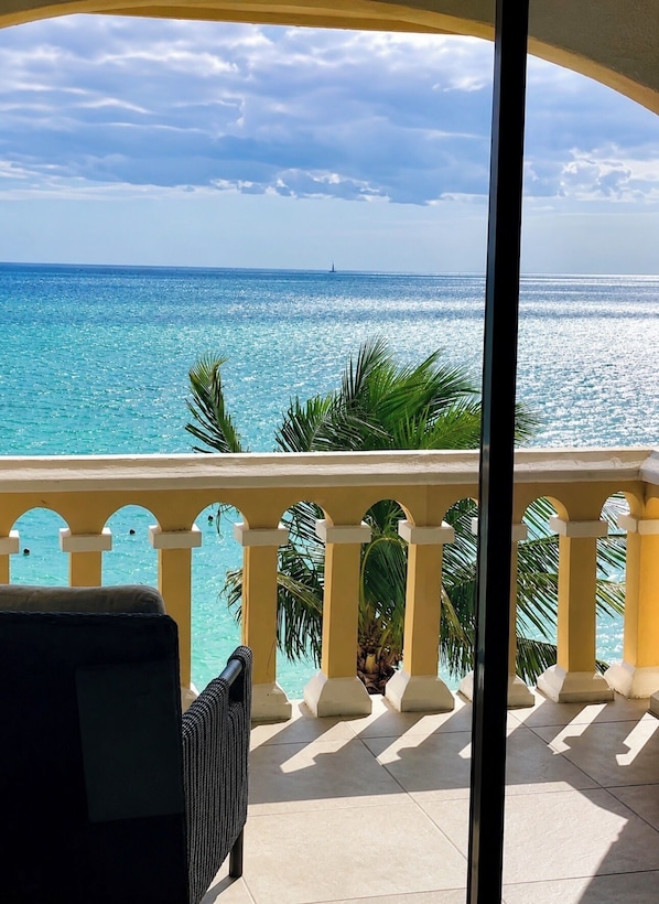 Un balcón con vista al océano, una silla y una palmera.
