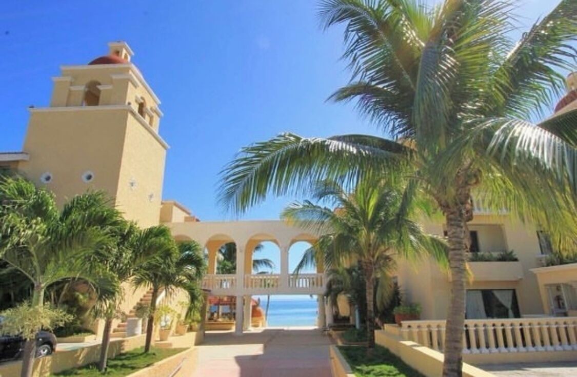 A resort with a central archway, palm trees, and a clear view of the ocean.