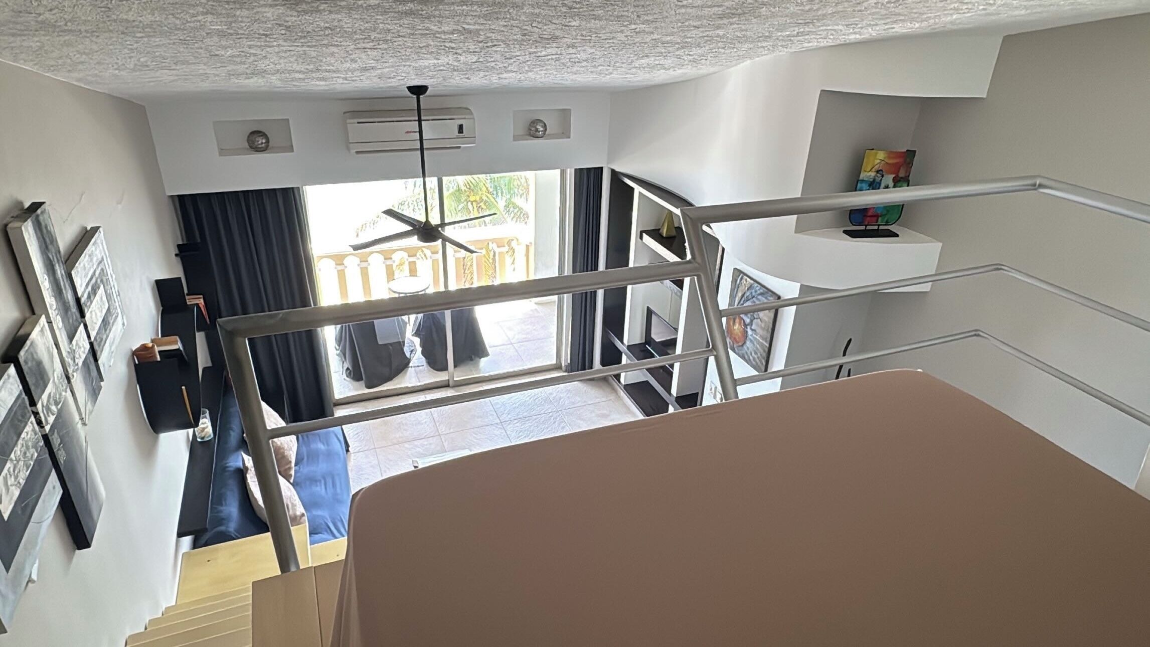 Een trap die leidt naar een balkon, met een plafondventilator, uitzicht op het buitengebied en een eettafel met stoelen.