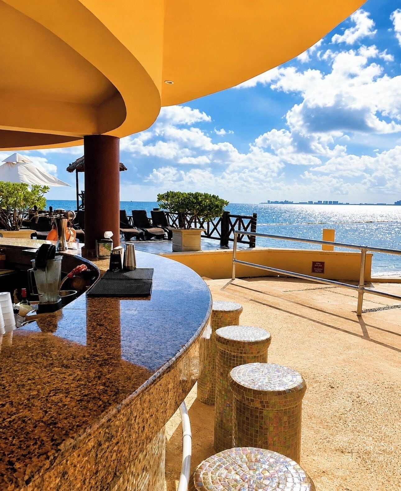 Eine Außenbar mit Meerblick, Sitzgelegenheiten und einem gefliesten Boden.
