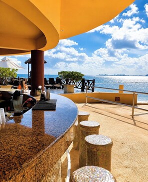 An outdoor bar area with a view of the sea, seating arrangements, and a tiled floor. - caribbean apartments (Cancún)