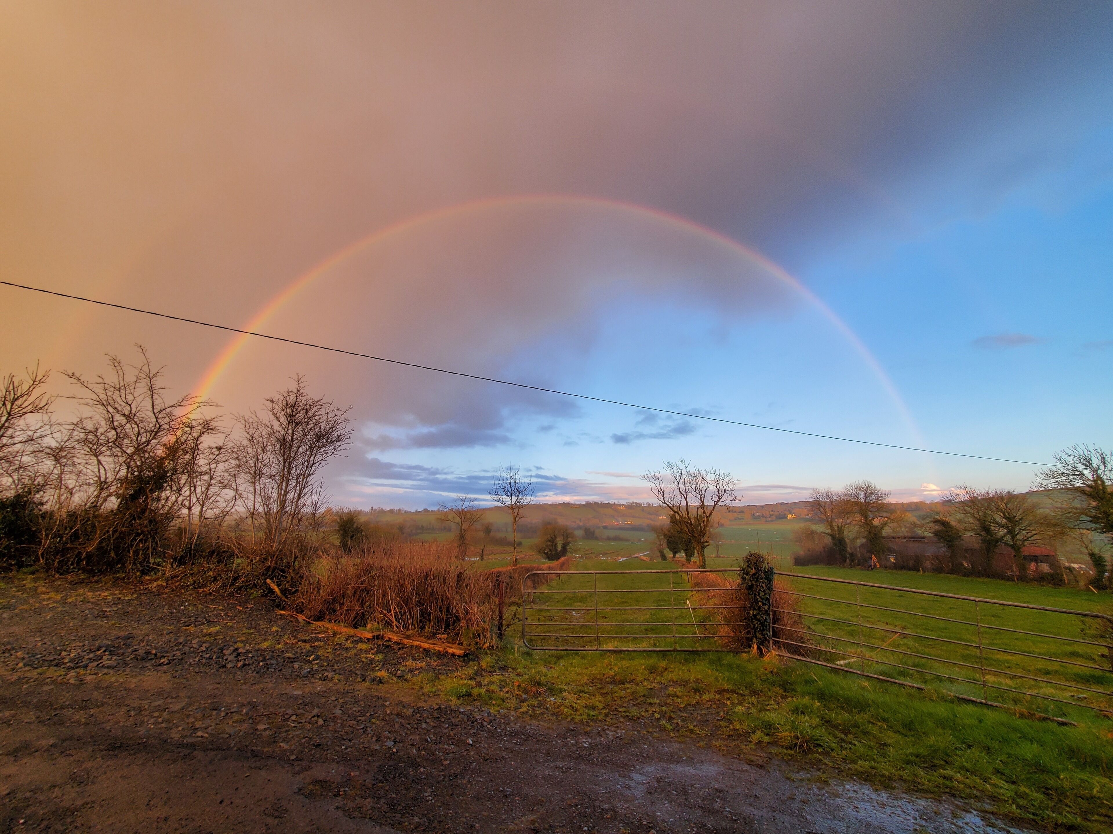 A rural landscape with a rainbow, open fields, and a fence.