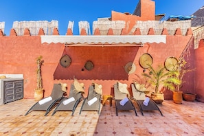 Terraza en la azotea con sillones de tomar el sol, plantas en macetas y un muro decorativo.