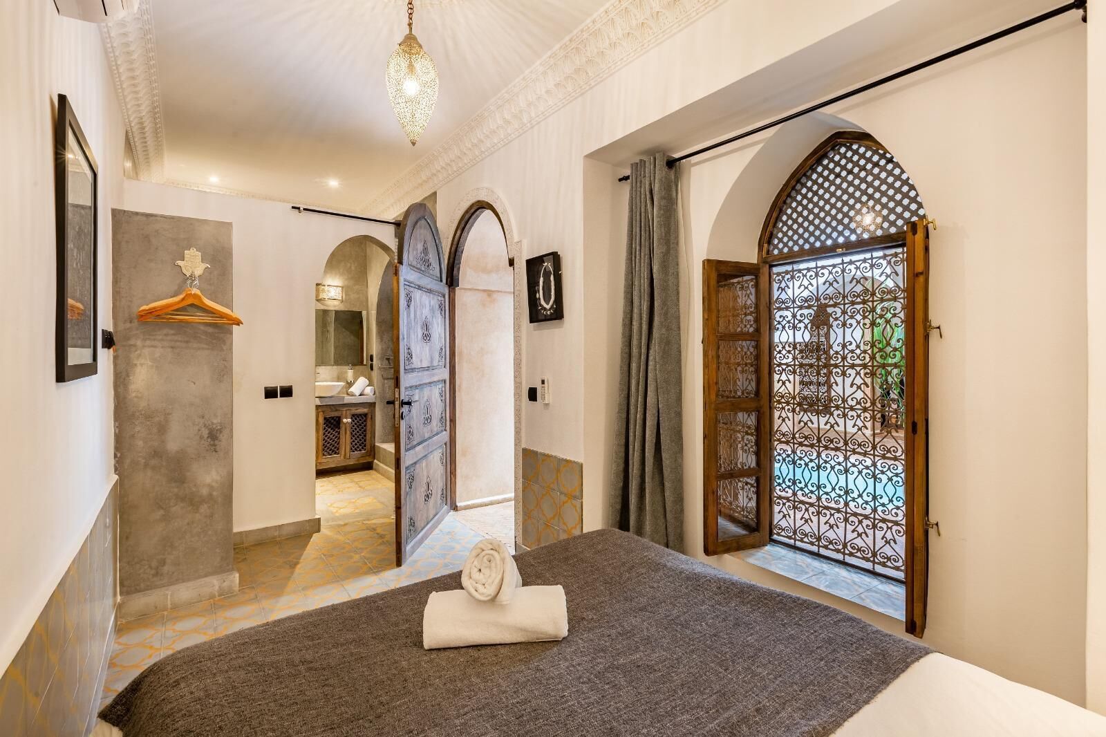 A bedroom with a large bed, a bathroom with a sink and mirror, and a view through a decorative door.