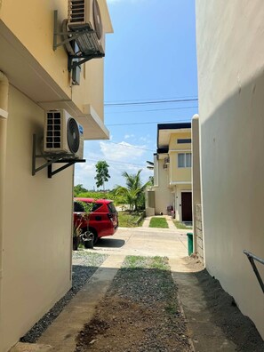 Um beco estreito com um carro vermelho estacionado na lateral, cercado por edifícios com aparelhos de ar condicionado.