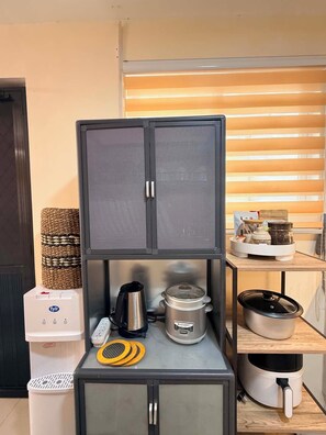 Uma cozinha compacta com micro-ondas, chaleira e cozedor de arroz em uma bancada.