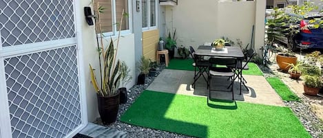 A residential outdoor space with a patio, a table with chairs, potted plants, and a green artificial turf area.