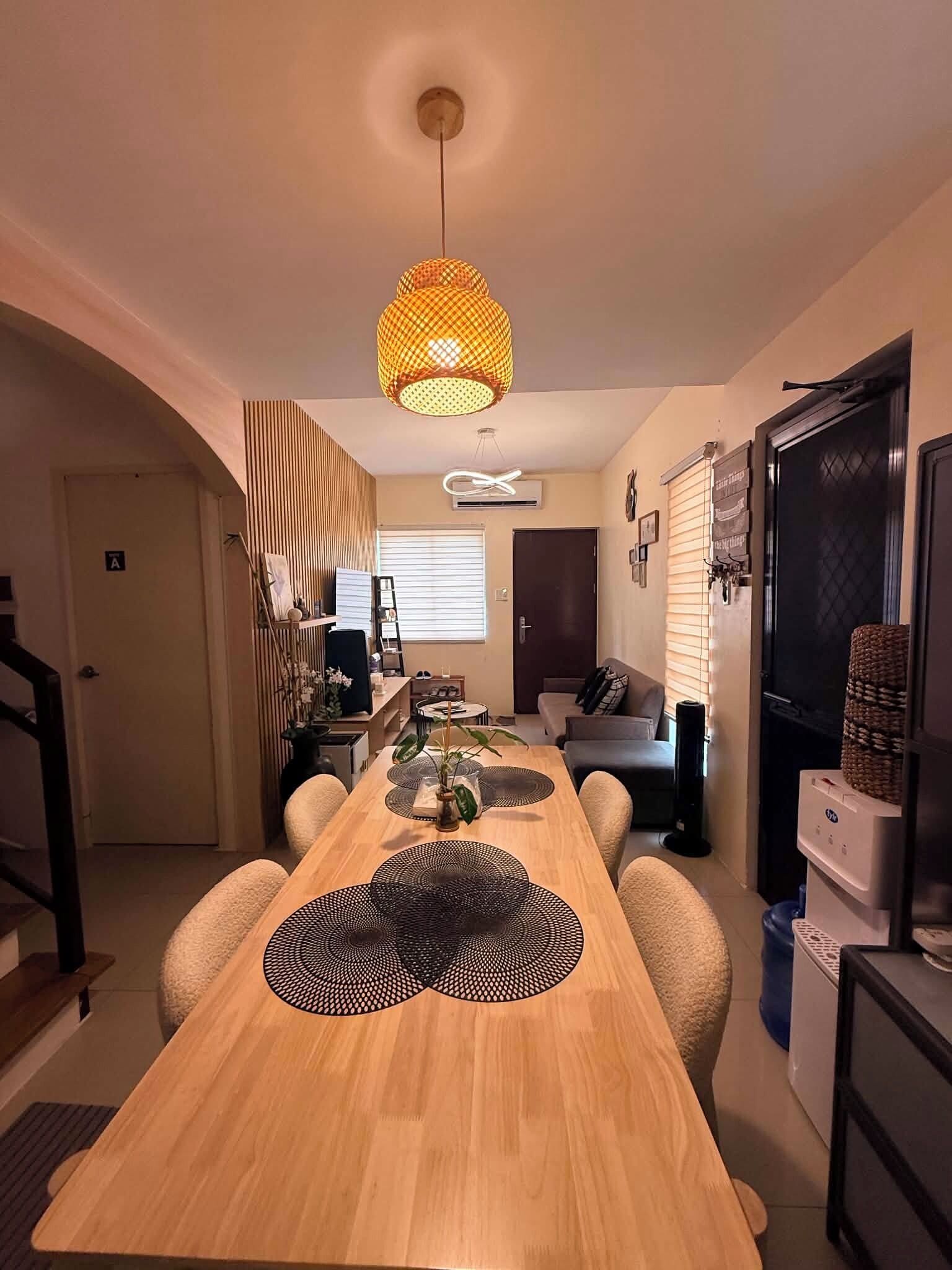 A modern kitchen with a wooden dining table, a hanging light fixture, and a refrigerator.