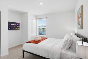 A bedroom with a bed, a nightstand, a wall-mounted TV, and a window with blinds.
