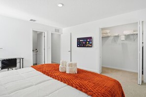 Quarto de hotel com cama, escrivaninha, televisão fixada na parede e armário.