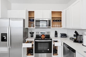 Een moderne keuken met witte kasten, een roestvrijstalen koelkast, een magnetron, een oven en een koffiehoek.