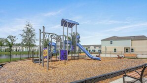 A playground with a slide and climbing structures, surrounded by a fence and a bench. - Posh 3BR Townhome| Pool | Gym | Close to Beach (St. Augustine)