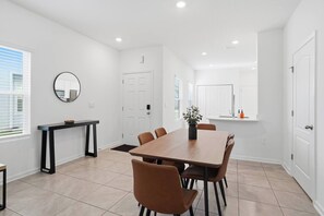 Een moderne eethoek met een houten tafel, stoelen, een klein bijzettafeltje en een potplant.