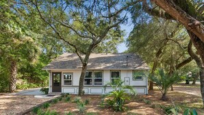 A single-story house with a front porch, surrounded by trees and a landscaped garden. - Point Me To Paradise (Pensacola)