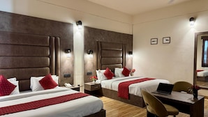 A hotel room with two beds, a desk, a chair, a laptop, a phone, and a ceiling fan. - Vella Vista Resort (dehradun)
