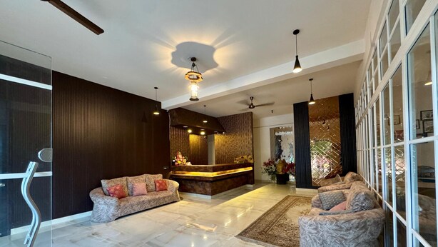 A modern lobby with a reception desk, two sofas, a ceiling fan, and a large glass door. - Vella Vista Resort (dehradun)