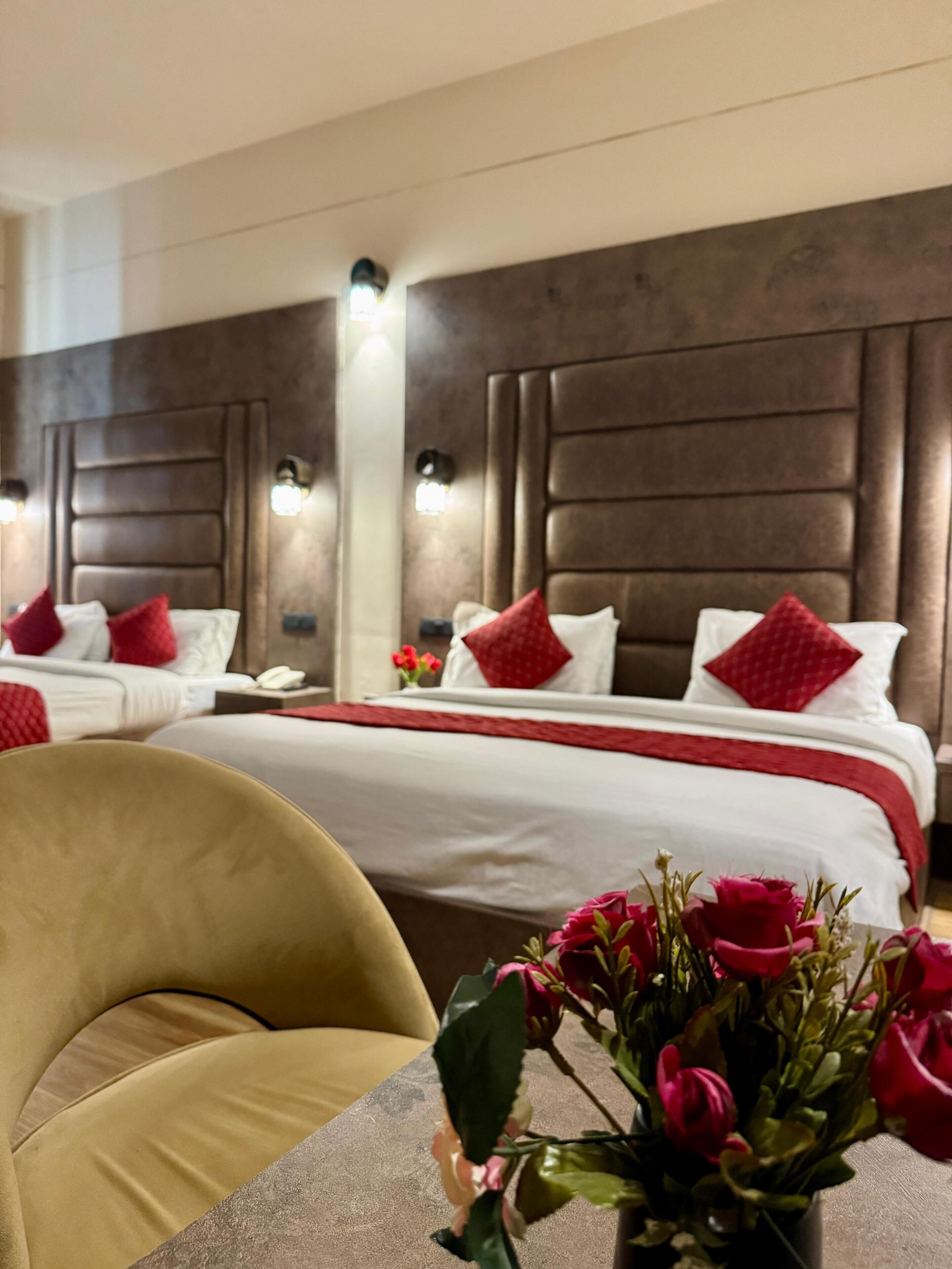 Habitación de hotel con una cama grande, dos mesitas de noche, una silla y un jarrón con flores.