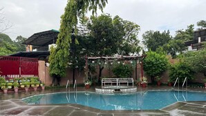 A swimming pool with a covered area, surrounded by potted plants and trees. - Vella Vista Resort (dehradun)