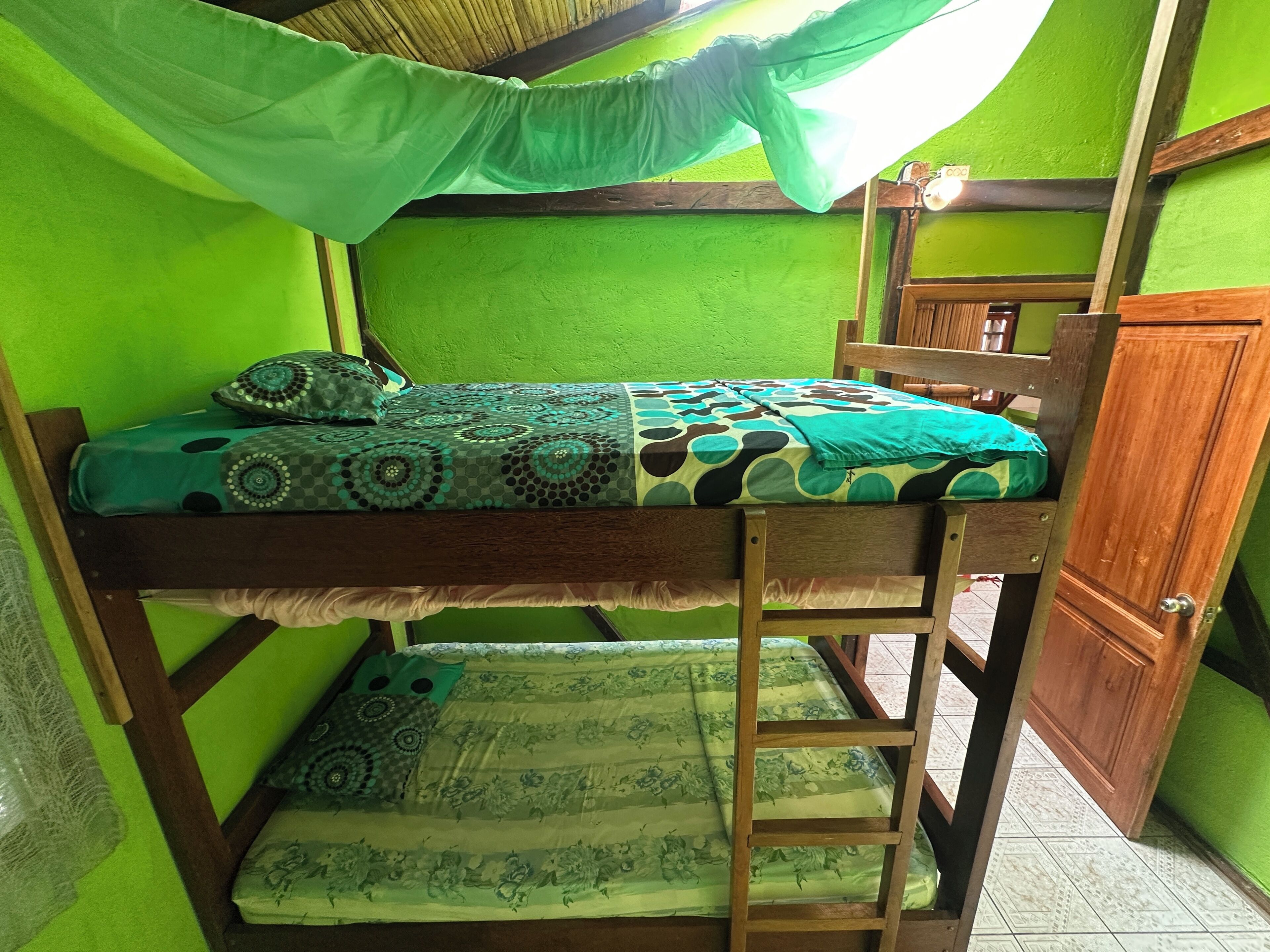 Een stapelbed met een groen hemeltje, een houten ladder en een groene muur.