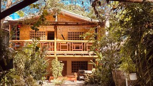 A rustic wooden building with a balcony, surrounded by dense foliage.