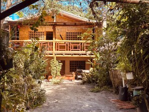 A rustic wooden building with a balcony, surrounded by dense foliage.