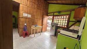 A kitchen with bamboo walls, a water dispenser, a refrigerator, and a gas stove.