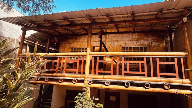 A traditional bamboo structure with a balcony, wooden railings, and a corrugated metal roof.