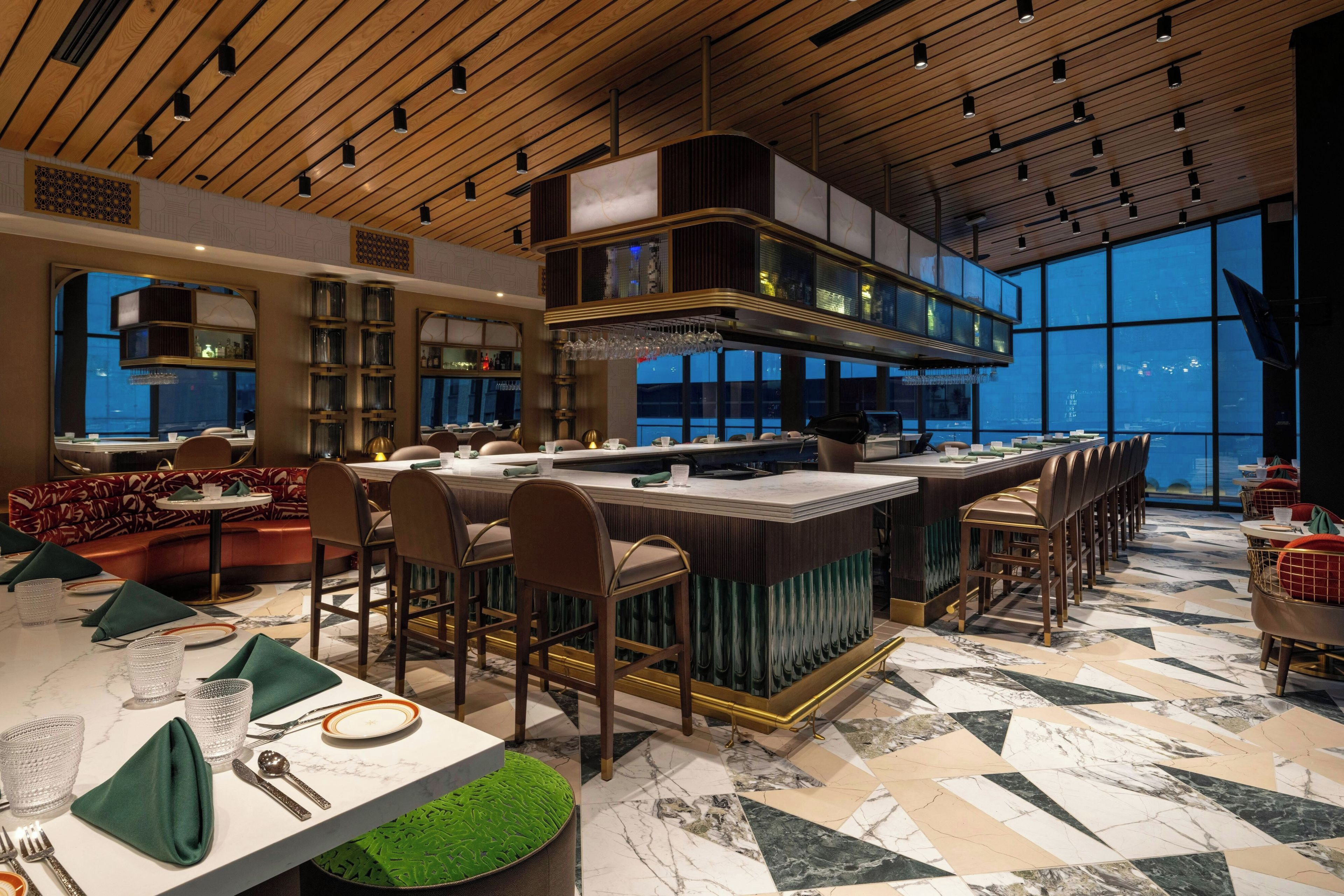 Un intérieur de restaurant moderne, avec un bar, des espaces aménagés pour s’asseoir et une vue dégagée grâce à de grandes fenêtres.