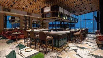 Un intérieur de restaurant moderne, avec un bar, des espaces aménagés pour s’asseoir et une vue dégagée grâce à de grandes fenêtres.