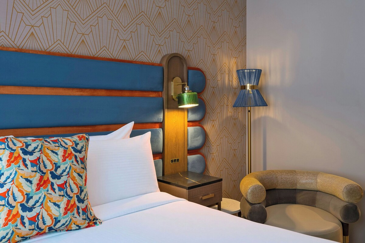 A hotel room with a bed, a nightstand, a lamp, and a chair.