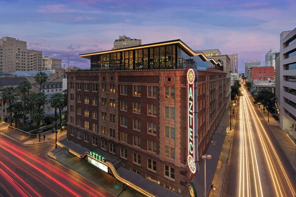 A multi-story building with a prominent neon sign, a flat roof, and a street with light trails. - Aztec Hotel, San Antonio, A Tribute Portfolio Hotel (San Antonio)