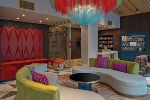 A modern lounge area with a curved sofa, a round coffee table, and a vibrant red wall with geometric patterns. - Aztec Hotel, San Antonio, A Tribute Portfolio Hotel (San Antonio)