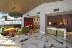 A hotel lobby with a modern design, featuring a large seating area with sofas and a coffee table, a patterned floor, and a view of the city through large windows.