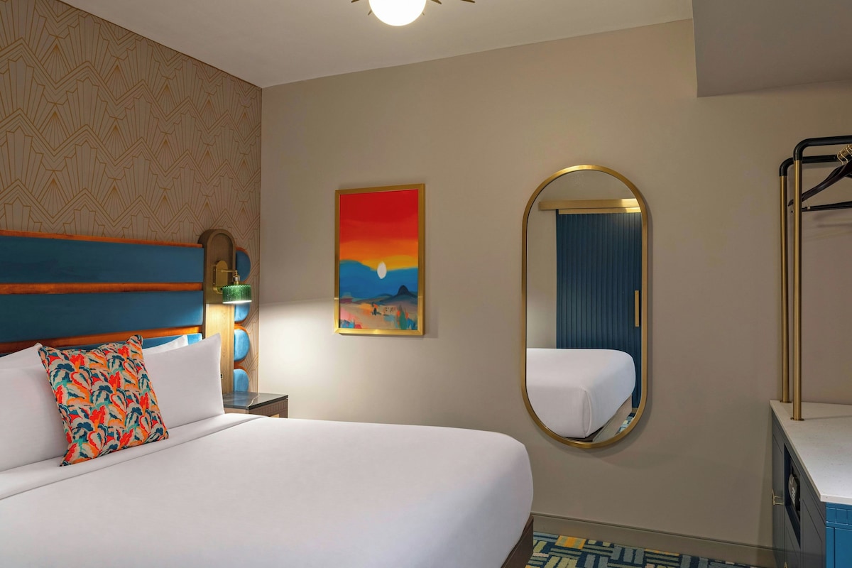 A hotel room with a bed, a large mirror, a painting, and a wardrobe.