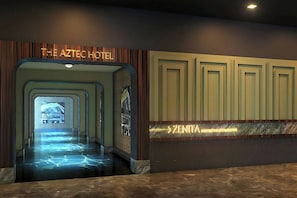 A hotel lobby with a neon sign for 'The Aztec Hotel' and a directional sign for 'ZENTIA HOTEL & SPA'.