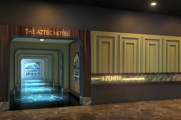 A hotel lobby with a neon sign for 'The Aztec Hotel' and a directional sign for 'ZENTIA HOTEL & SPA'.