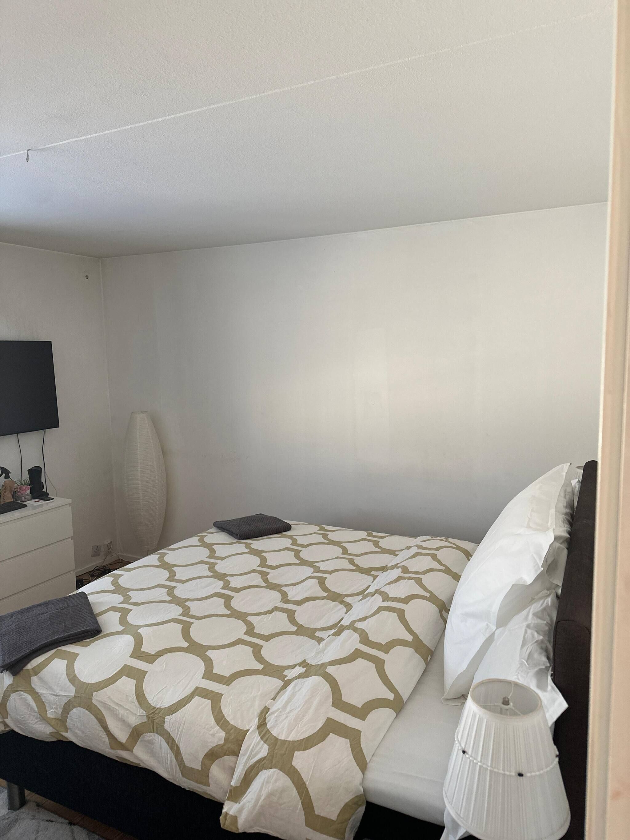 A neatly made bed with a patterned bedspread, a bedside lamp, and a flat-screen TV on a white dresser.