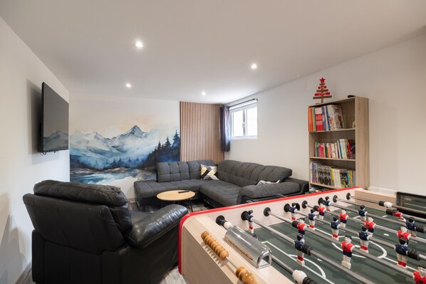 Una sala de estar moderna con una mesa de fútbol de mesa, un sofá, una estantería y un cuadro de montañas.