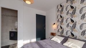 A bedroom with a bed, a nightstand, a wall-mounted lamp, and a bathroom with a towel rack.