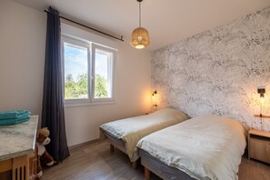 Un dormitorio con dos camas, una ventana con cortinas, una lámpara de pared y una mesita de noche de madera.