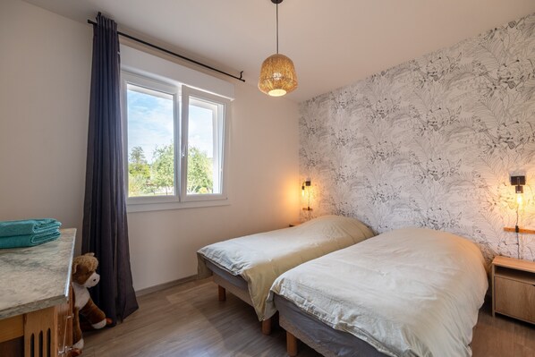 Une chambre avec deux lits, une fenêtre avec des rideaux, une lampe fixée au mur et une table de chevet en bois.