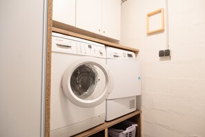 Une petite buanderie équipée d’un lave-linge Bosch, d’un sèche-linge et d’une étagère en bois.