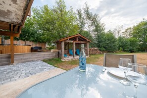 Un patio trasero con una mesa de vidrio, sillas, una pérgola y un gazebo de madera.