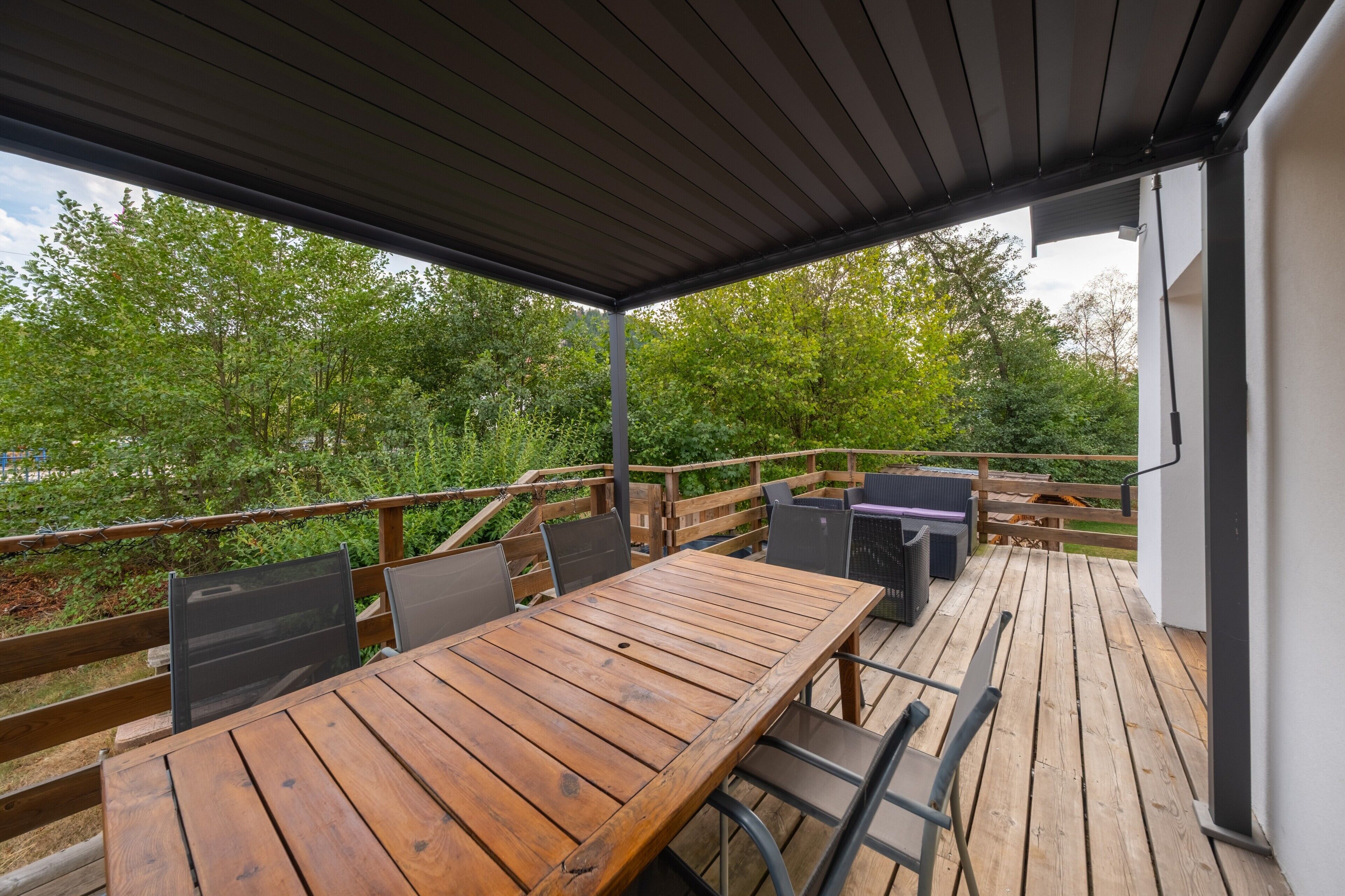 Une terrasse extérieure avec une table et des chaises en bois, un barbecue et une vue sur la verdure.