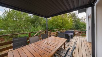 Une terrasse extérieure avec une table et des chaises en bois, un barbecue et une vue sur la verdure.
