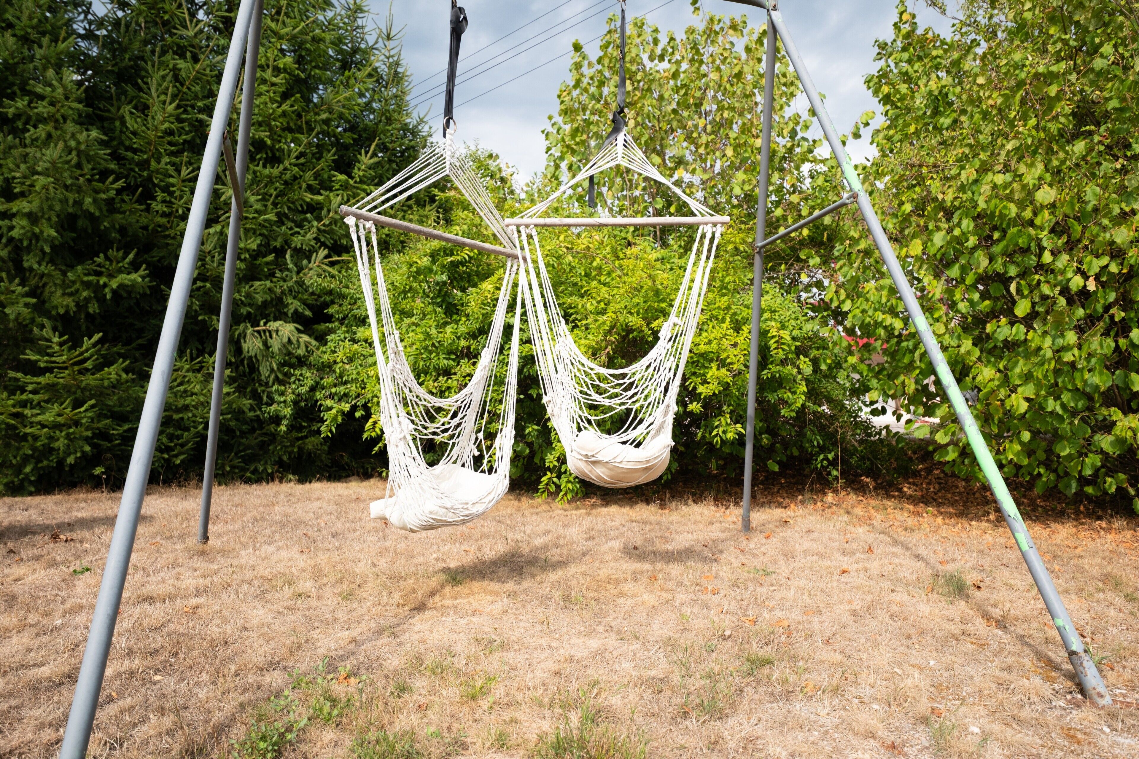 A hammock swing set in a grassy area with trees in the background.